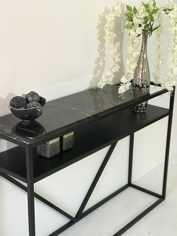 console design avec plateau en marbre noir, pied et étagère en métal noir laqué