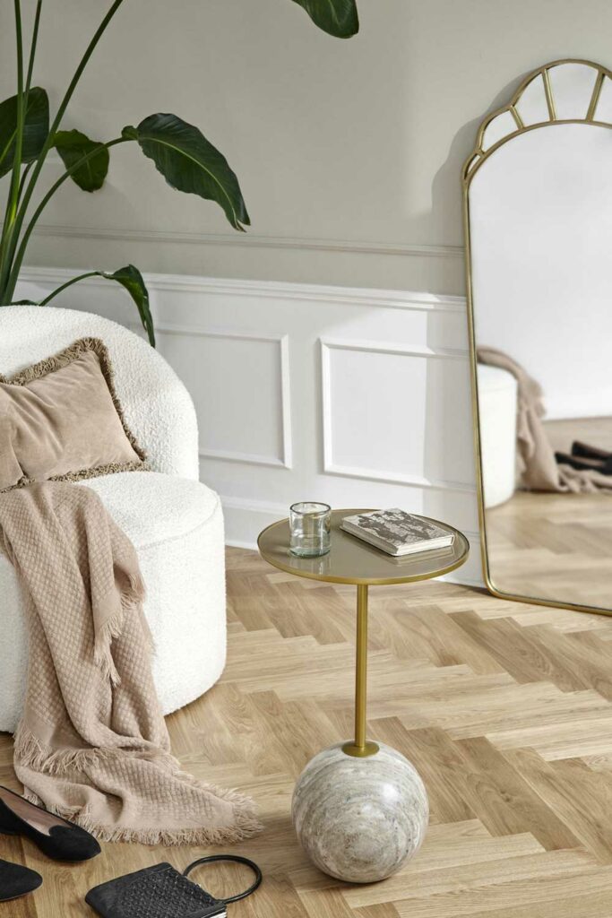 Fauteuil lounge en tissu bouclette blanc avec un coussin, un plaid beige, à côté duquel se trouve une table d'appoint en marbre