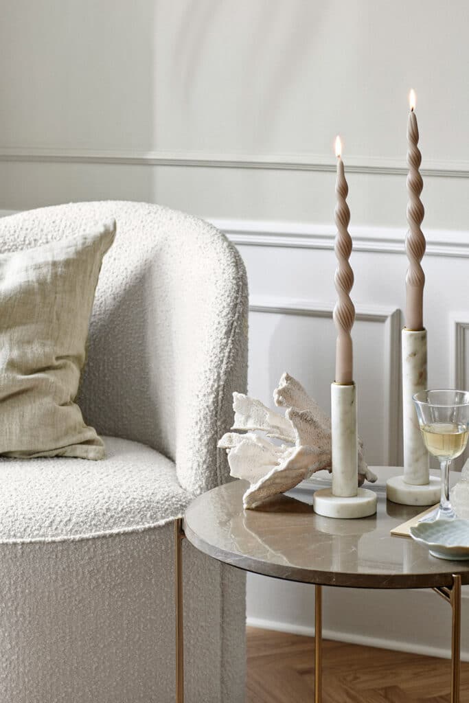 Fauteuil Lounge de salon, blanc à côté duquel se trouve une table d'appoint en marbre clair avec bougeoirs et bougies chandelles.
