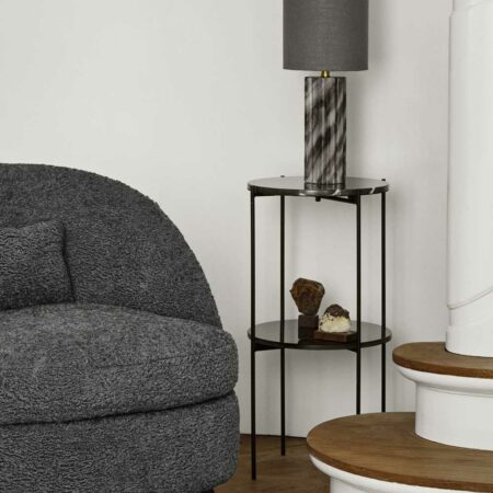 sellette ronde de type console avec 2 étagères : une en marbre noir et l'autre en verre noir. Elle est associée à un fauteuil Louge gris et une Lampe en marbre gris.