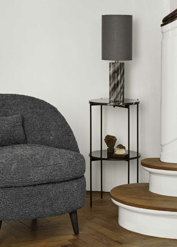 sellette ronde de type console avec 2 étagères : une en marbre noir et l'autre en verre noir. Elle est associée à un fauteuil Louge gris et une Lampe en marbre gris.
