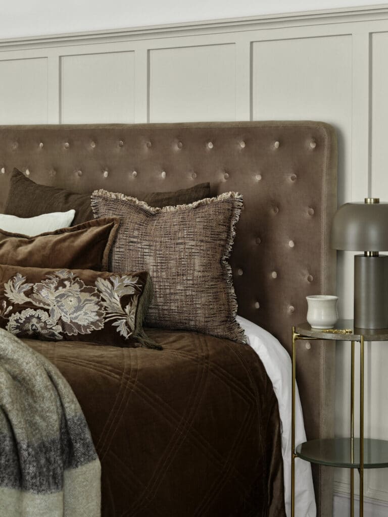 Table de chevet ronde en marbre à côté de son lit matrimonial avec dominante de couleur brun marron.