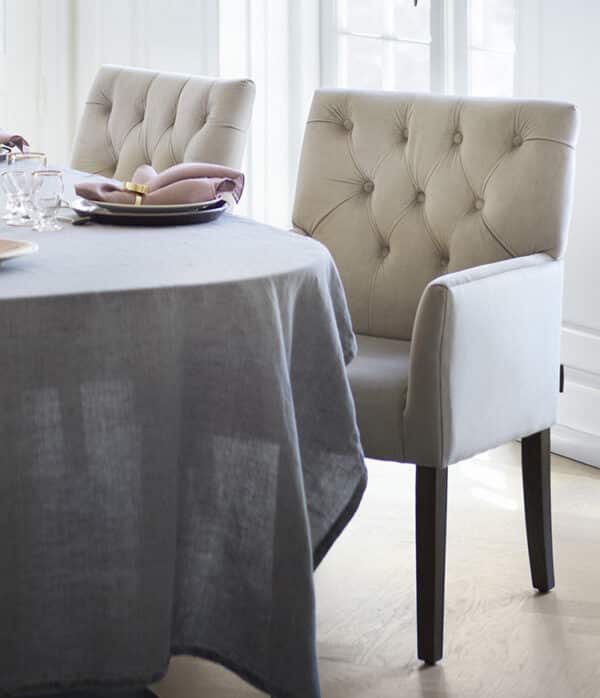 Table à manger dressée avec nappe grise et chaises élégantes avec accoudoirs, en velours beige.